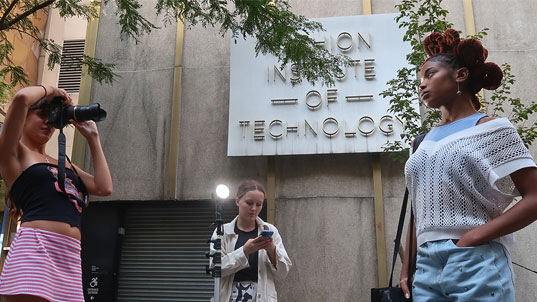 A female student taking a photo of a female model outside of FIT