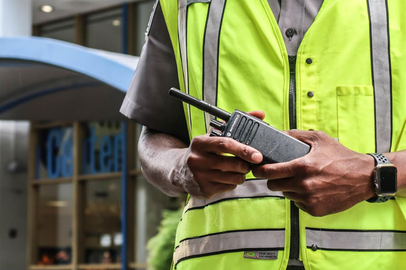 Security guard standing in a neon yellow vest holding a walkie talkie