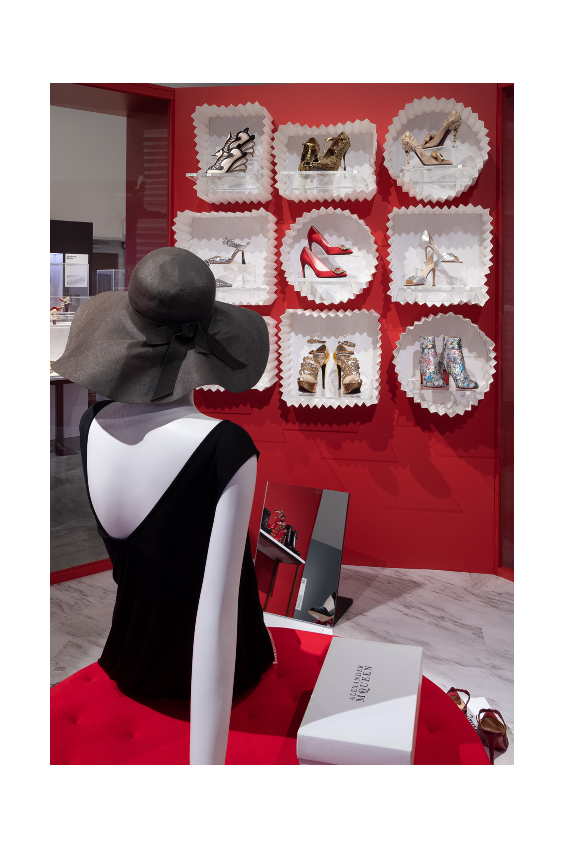 Shoes installation of a mannequin wearing a black hat and dress sitting inside a red shoe "candy shop" boutique