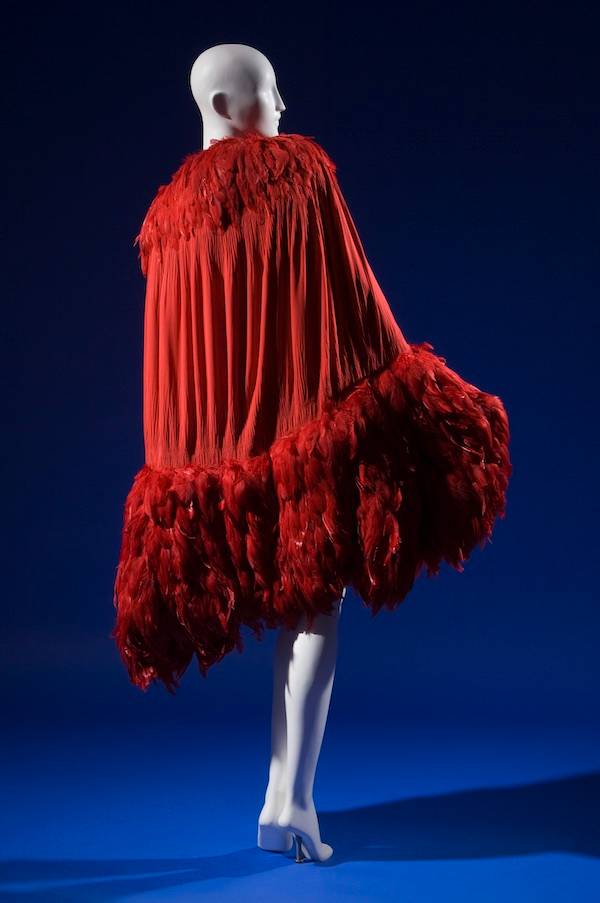 calf length evening cape in doubled red silk crepe de chine crinkled and smocked along curved edges of cocoon silhouette, crimson feather trim forming shawl collar and wide hem band