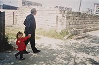 young girl in red jacket holding hands with adult male while walking down the street